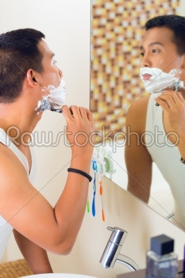 Asian man shaving in front of mirror