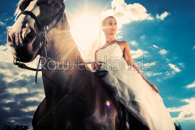 Bride in wedding dress riding a horse, backlit