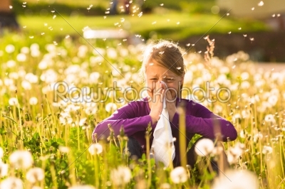 Girl sitting in meadow with dandelions and has hay fever or allergy