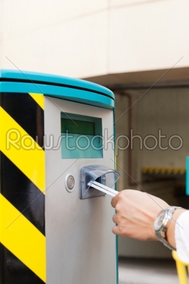 Hand is _insert_ing parking ticket into barrier of garage