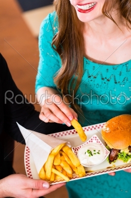 Friends or couple eating fast food with burger and fries 