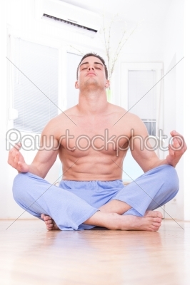 young handsome muscular  half naked man doing yoga and meditating indoors in living room