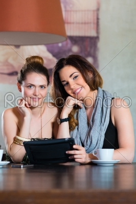 Young women or colleagues sitting in a cafe or restaurant, and looking on the Tablet Computer